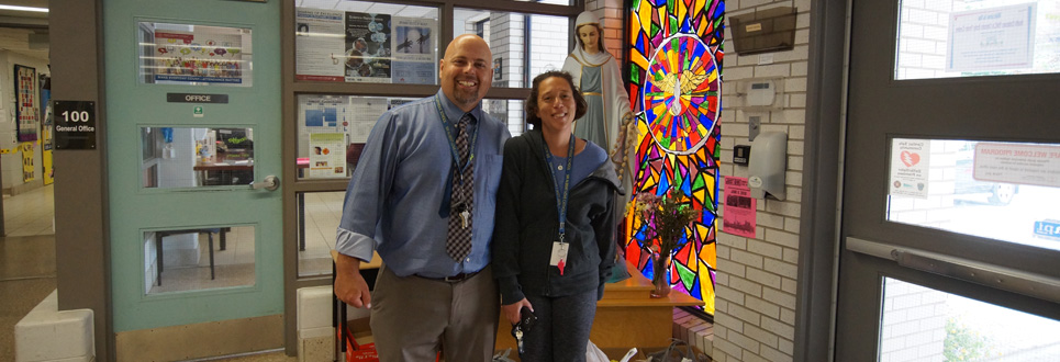 Two parent volunteers in front of the Mary statue and a multi-coloured stained glass window